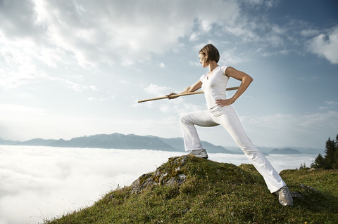 Austria, Kranzhorn, Mid adult woman exercising stick fighting on mountain top stock photo