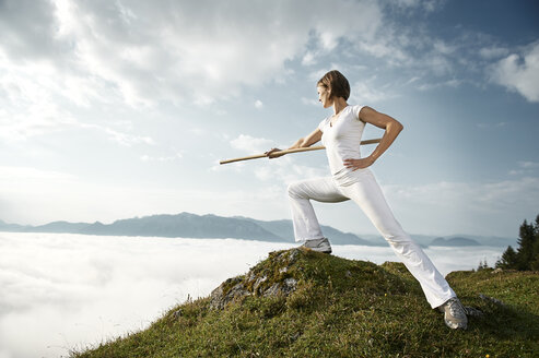 Austria, Kranzhorn, Mid adult woman exercising stick fighting on mountain top - MAOF000058