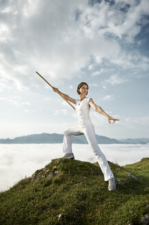 Austria, Kranzhorn, Mid adult woman exercising stick fighting on mountain top - MAOF000059