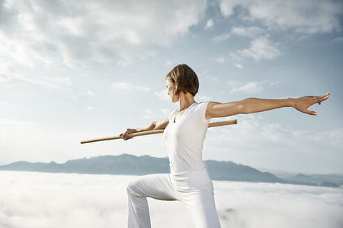 Austria, Kranzhorn, Mid adult woman exercising stick fighting on mountain top - MAOF000060