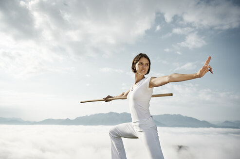 Austria, Kranzhorn, Mid adult woman exercising stick fighting on mountain top - MAOF000061