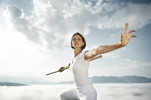 Austria, Kranzhorn, Mid adult woman exercising stick fighting on mountain top - MAOF000062