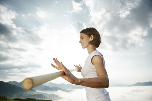 Austria, Kranzhorn, Mid adult woman exercising stick fighting on mountain top - MAOF000005