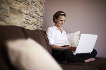 Woman sitting cross-legged on couch using laptop - MAOF000014