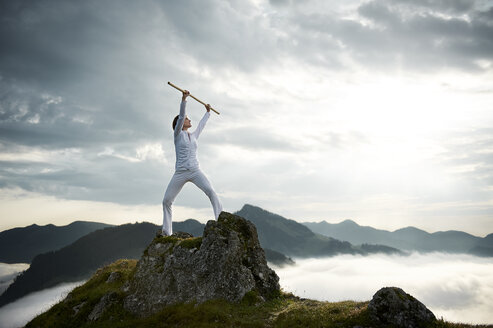 Austria, Kranzhorn, Mid adult woman exercising stick fighting on mountain top - MAOF000031