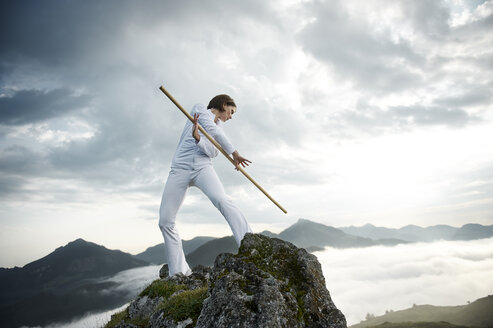 Austria, Kranzhorn, Mid adult woman exercising stick fighting on mountain top - MAOF000032