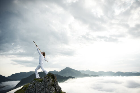 Austria, Kranzhorn, Mid adult woman exercising stick fighting on mountain top - MAOF000034