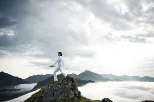 Austria, Kranzhorn, Mid adult woman exercising stick fighting on mountain top - MAOF000035