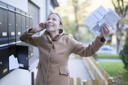 Glückliche Frau telefoniert mit Smartphone und hält einen Brief in der Hand - NNF000199