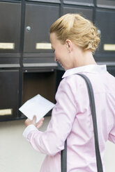 Frau vor einem Briefkasten stehend, die den Brief betrachtet - NNF000201