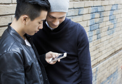 China, Hongkong, young male gay couple standing in street looking at smartphone - JUBF000014