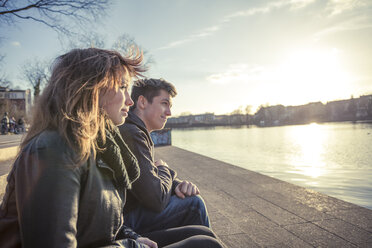 Germany, Berlin, teenage couple sitting at lakeshore in the late afternoon - MMFF000530