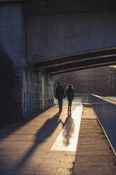 Deutschland, Berlin, jugendliches Paar geht unter einer Brücke bei Abendsonne - MMFF000527