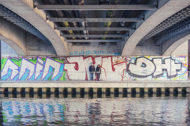 Deutschland, Berlin, jugendliches Paar lehnt an Graffiti-Wand unter einer Brücke - MMFF000516