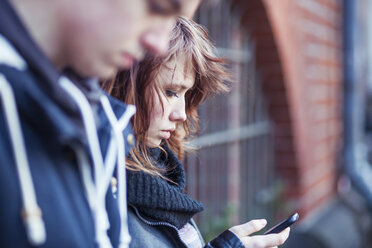 Teenager-Mädchen mit Smartphone, Junge unscharf im Vordergrund - MMFF000511