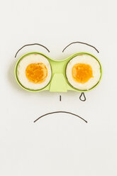 Zwei Hälften eines Eies in einem grünen Halter mit einem traurigen Gesicht, das um das Ei herum gezeichnet ist - MELF000049