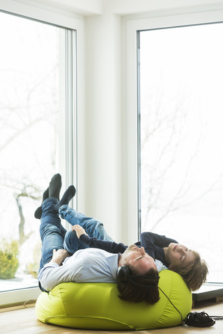 Father and son lying on bean bag in living room listening music stock photo