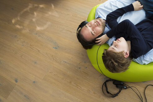 Father and son lying on bean bag in living room listening music - JTLF000069
