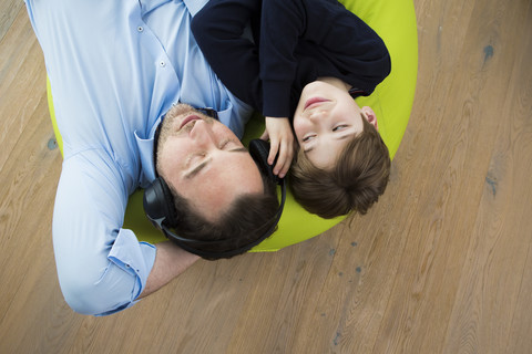 Father and son lying on bean bag in living room listening music stock photo