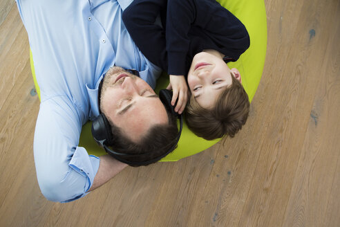 Father and son lying on bean bag in living room listening music - JTLF000071