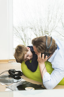 Father and son lying on bean bag in living room listening music - JTLF000073