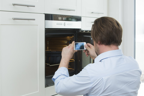 Man photographing cake in the oven with smartphone stock photo