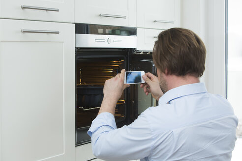 Man photographing cake in the oven with smartphone - JTLF000076