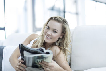Porträt einer blonden Frau auf einer Couch liegend mit einer Zeitschrift - ZEF003624