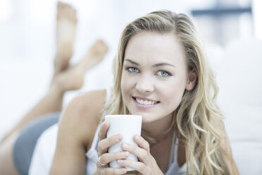 Porträt einer blonden Frau auf einer Couch liegend mit einer Tasse Kaffee - ZEF003627