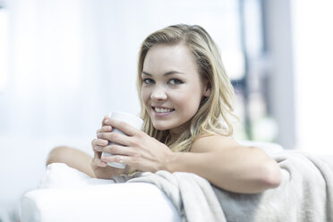 Portrait of blond woman sitting on a couch with cup of coffee - ZEF003628