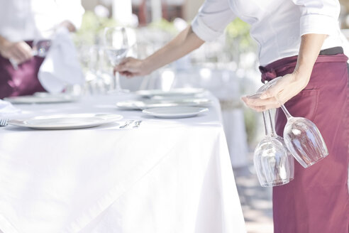 Waiter placing wine glasses on outdoor restaurant table - ZEF004024