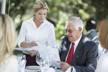 Waitress explaining menu to clients at table - ZEF004322