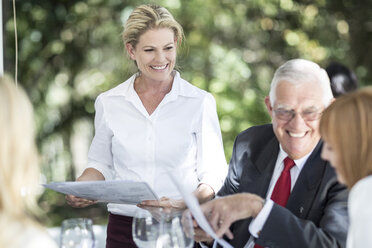 Waitress explaining menu to clients at table - ZEF004114