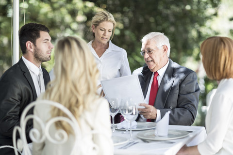 Die Kellnerin erklärt den Kunden am Tisch das Menü, lizenzfreies Stockfoto