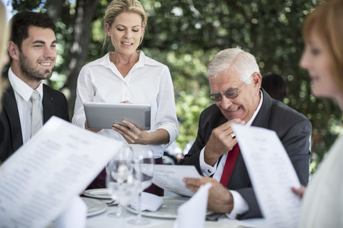 Kellnerin, die mit Hilfe eines digitalen Tablets die Mittagsbestellungen der Kunden am Tisch aufnimmt, lizenzfreies Stockfoto