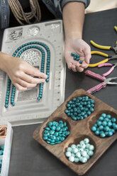 Nahaufnahme einer Frau, die mit Perlen arbeitet, um eine Halskette herzustellen - ZEF003638