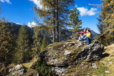 Austria, Altenmarkt-Zauchensee, young couple sitting on a rock looking at view - HHF005156