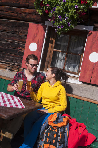 Austria, Altenmarkt-Zauchensee, young couple with beer glasses sitting in front of Alpine cabin stock photo