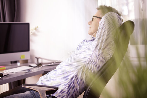 Businessman having a rest at home office hearing music with ear phones - SEGF000270