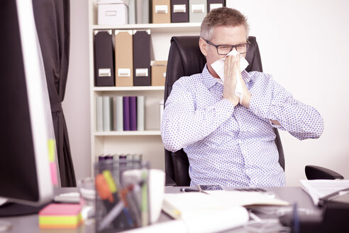 Businessman blowing nose at home office - SEGF000264