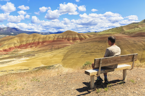 USA, Oregon, John Day Fossil Beds National Monument, Tourist sitzt auf einer Bank und schaut auf die Painted Hills, lizenzfreies Stockfoto