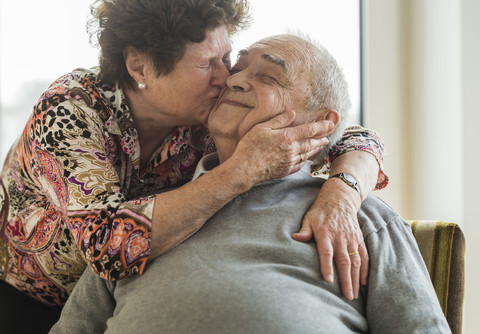 Ältere Frau umarmt und küsst ihren Mann, lizenzfreies Stockfoto