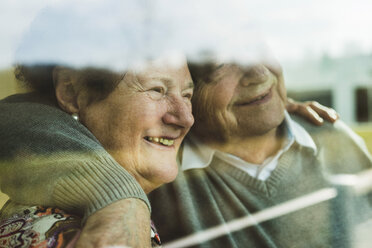 Glückliches älteres Paar, das Kopf an Kopf durch ein Fenster schaut - UUF003571
