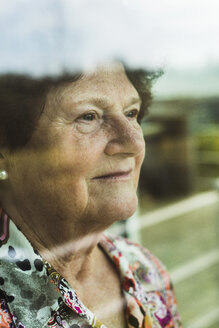 Porträt einer älteren Frau, die durch ein Fenster schaut - UUF003572