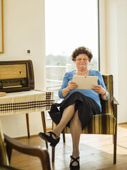 Porträt einer älteren Frau, die zu Hause ein digitales Tablet benutzt - UUF003584