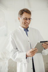 Smiling mature man in lab coat looking at digital tablet - MFF001542