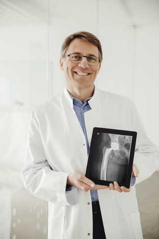 Älterer Mann im Laborkittel präsentiert einen Röntgenscan auf seinem digitalen Tablet, lizenzfreies Stockfoto