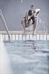 Swimmer in indoor pool sitting on starting block - ZEF004724