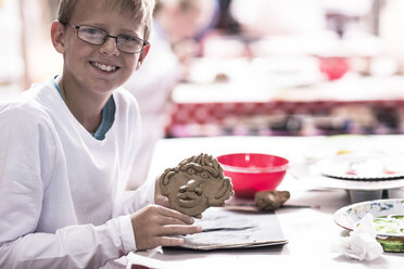 Lächelnder Junge, der im Kunstunterricht in der Schule ein Gesicht aus Knetmasse modelliert - ZEF006135