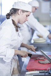 Teenage girl in kitchen cooking class cutting food - ZEF005947